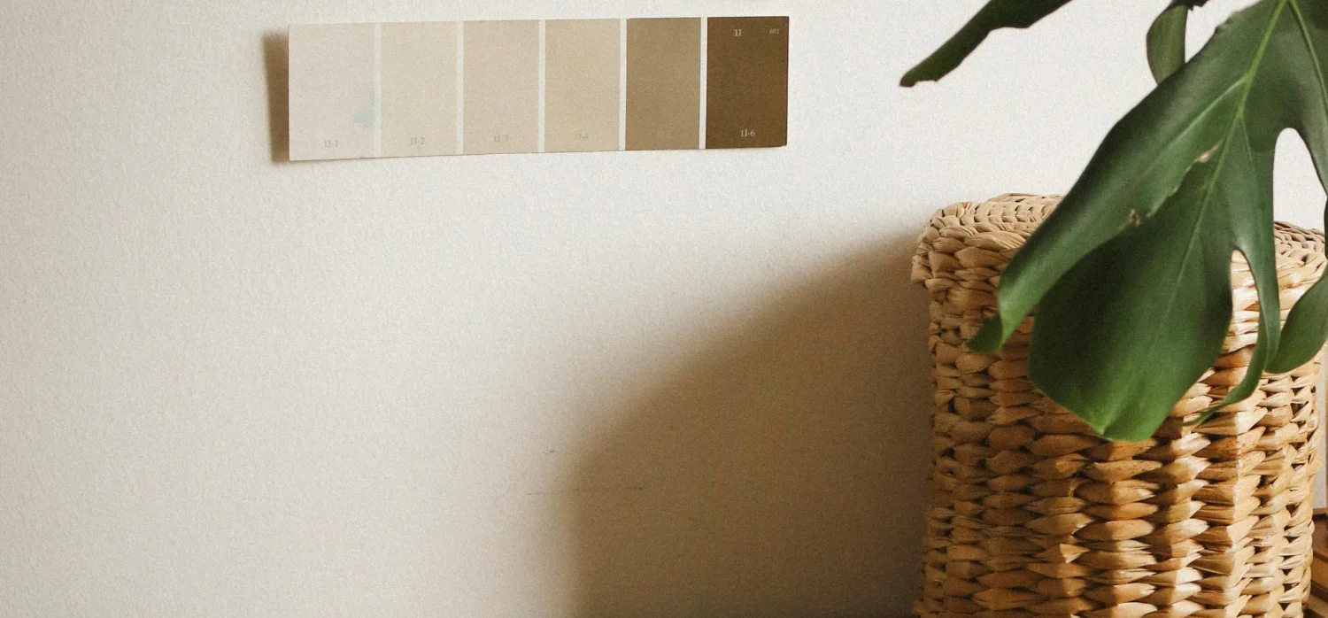 Échantillons de couleurs de peinture collés au mur et des pinceaux et un rouleau posés sur un meuble.