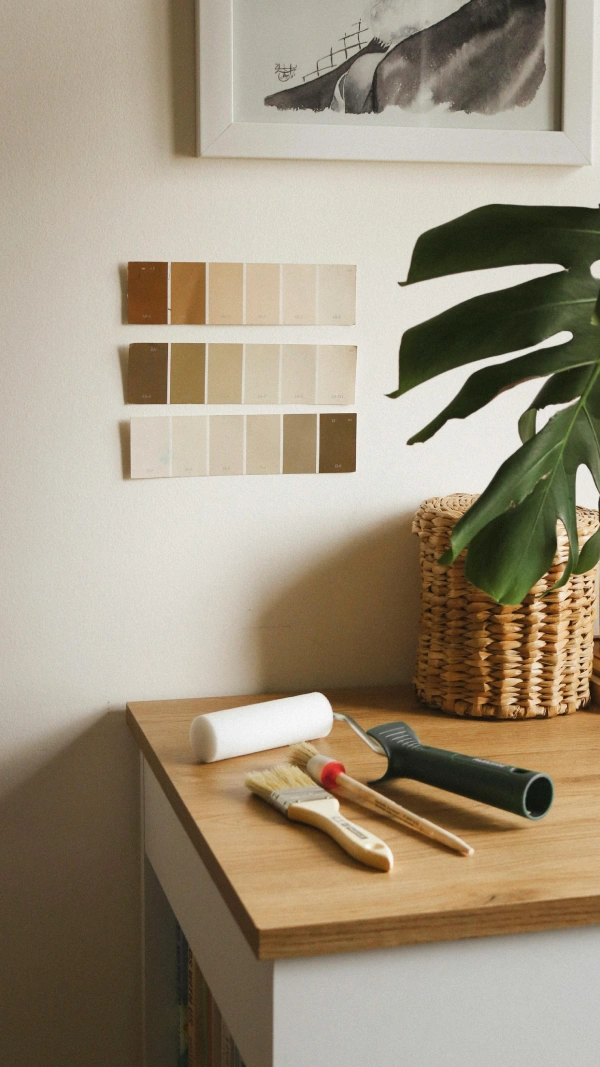 Échantillons de peinture collés sur le mur, et des pinceaux et un rouleau posés sur un meuble.