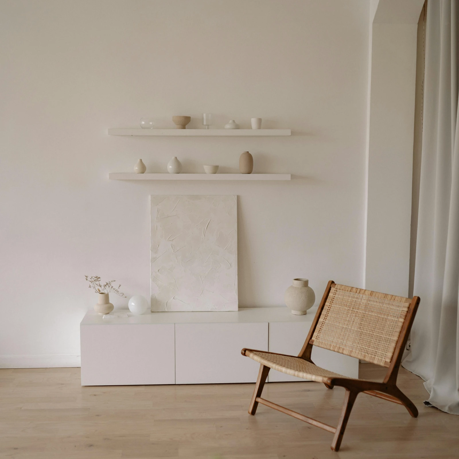Décoration style japandi, minimaliste et apaisant, meuble avec un vase en céramique une toile texturée et un fauteuil en bois et rotin.