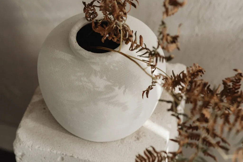 Décoration japandi authentique, minimaliste et naturelle, vase en céramique blanc avec fleurs séchées brunes.