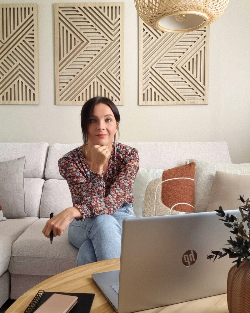 Photo de Sarah GUILLOT, joyeuse et souriante dans un salon chaleureux et cocooning, prête à accompagner mes clients. Décoratrice et designer d'espaces dans la Marne, spécialisée dans le bien-être chez soi.