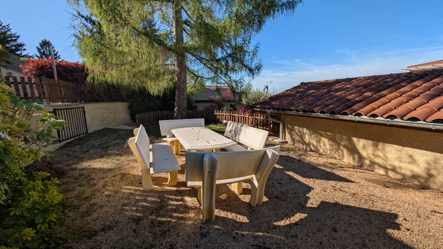 Terrasse aménagée ensoleillée avec table en pierre et végétation.