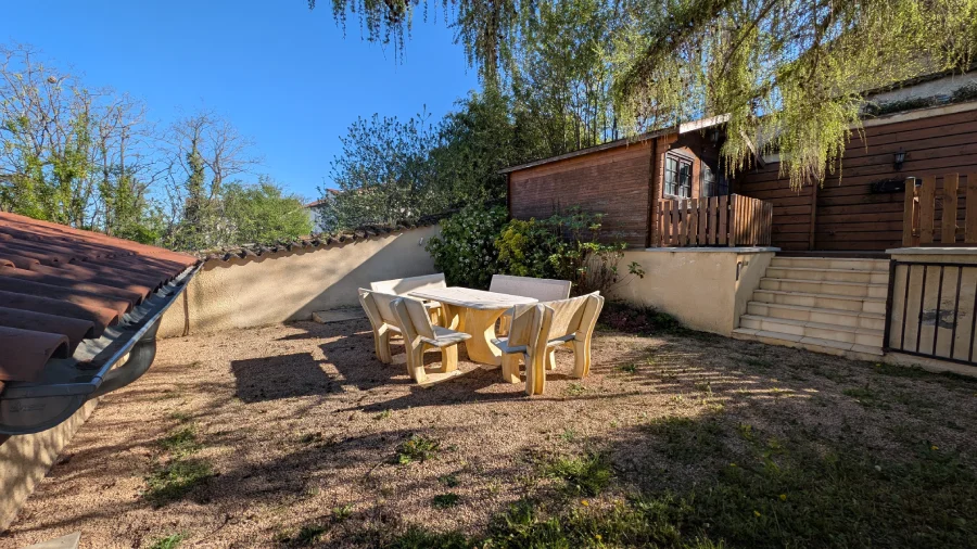 Terrasse aménagée ensoleillée avec table en pierre et végétation.